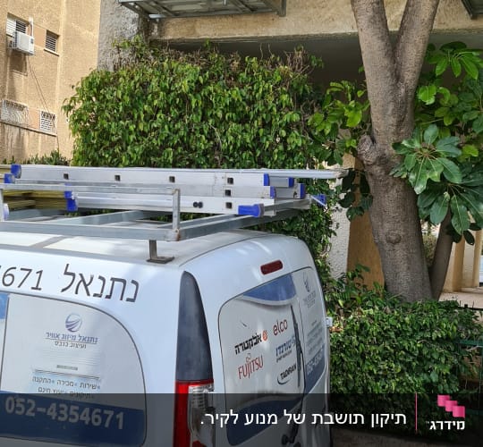 יחידת מיזוג אוויר מותקנת על קיר חיצוני ליד עץ